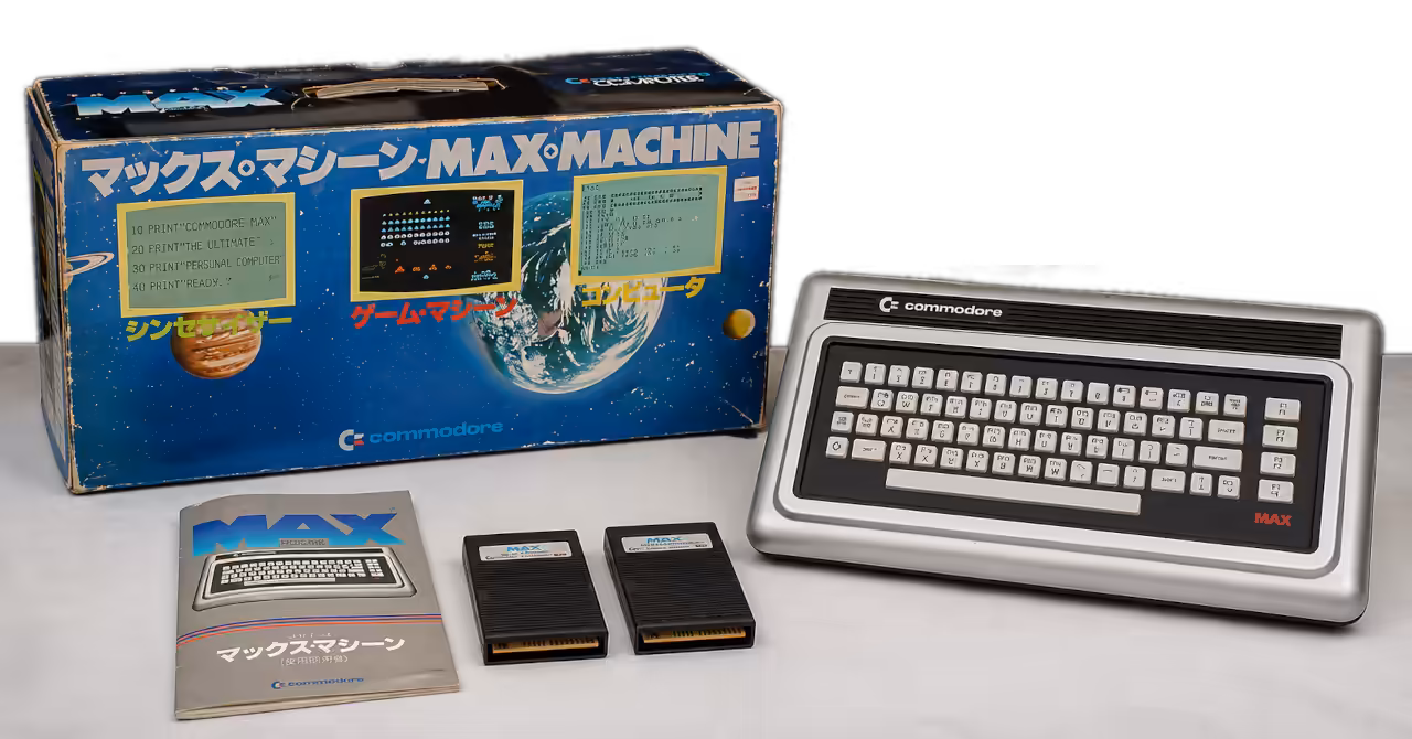 Commodore MAX Machine home computer displayed alongside its original Japanese retail packaging, instruction manual and software cartridges, illustrating one of Commodore's rarest consumer computers from 1982.