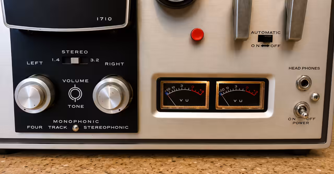 Close-up of the AKAI 1710W control panel showing illuminated dual VU meters, volume and tone controls, transport levers and headphone socket.